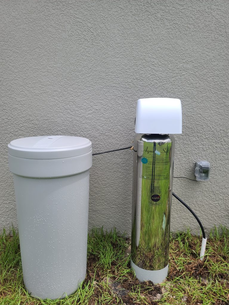 Outdoor water softener tanks beside stucco wall